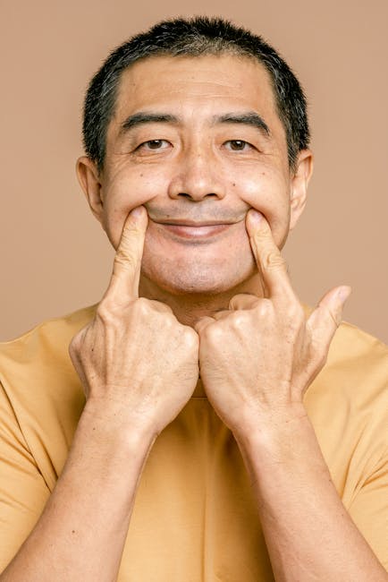 Elderly man in a casual t-shirt smiling with hands on his face against a brown backdrop.