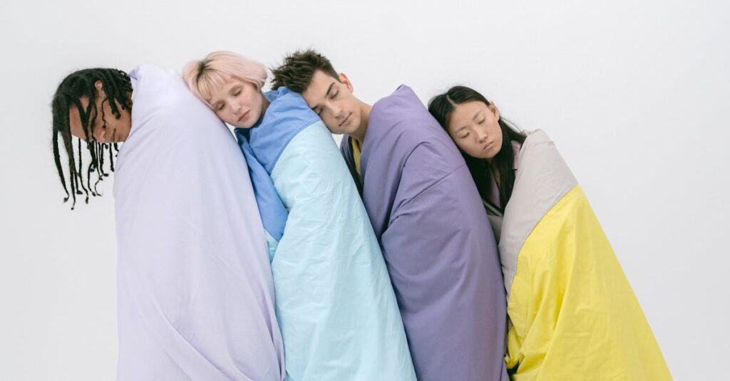 Four young adults standing wrapped in colorful quilts, eyes closed, against a white studio background.