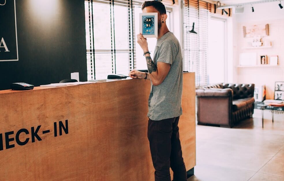 Man standing at a reception desk, holding a book, in a modern hotel lobby.
