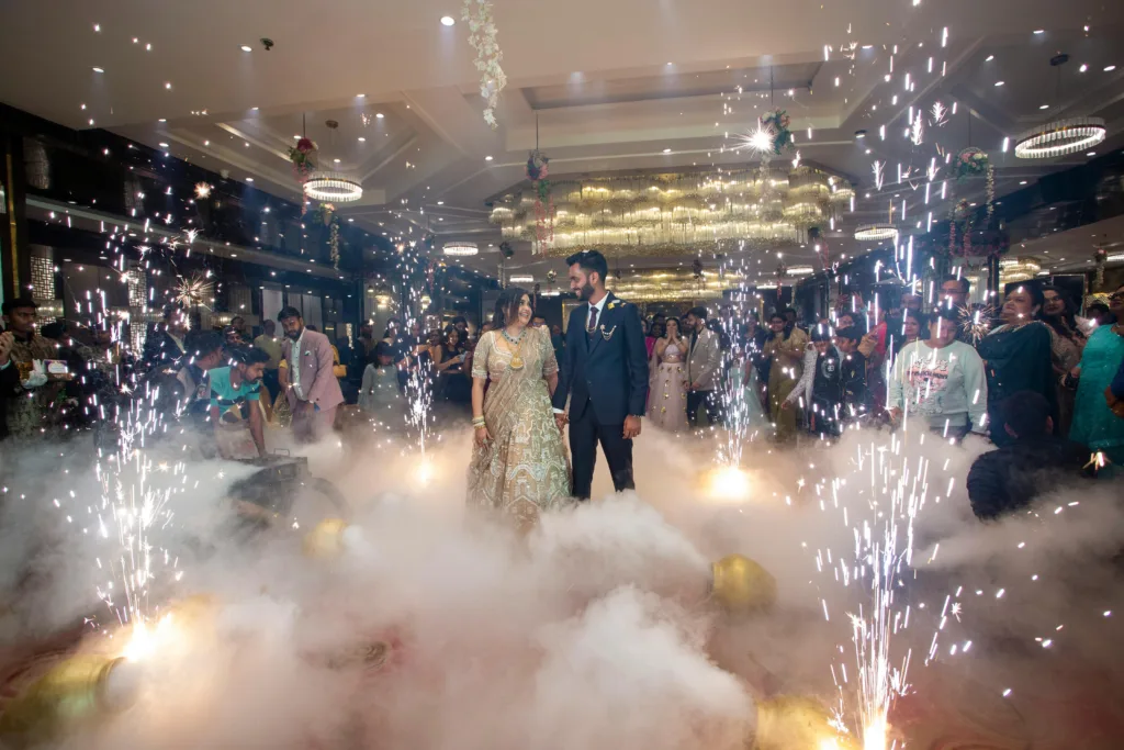 Bride and groom celebrating their wedding with guests amidst sparklers and smoke indoors.