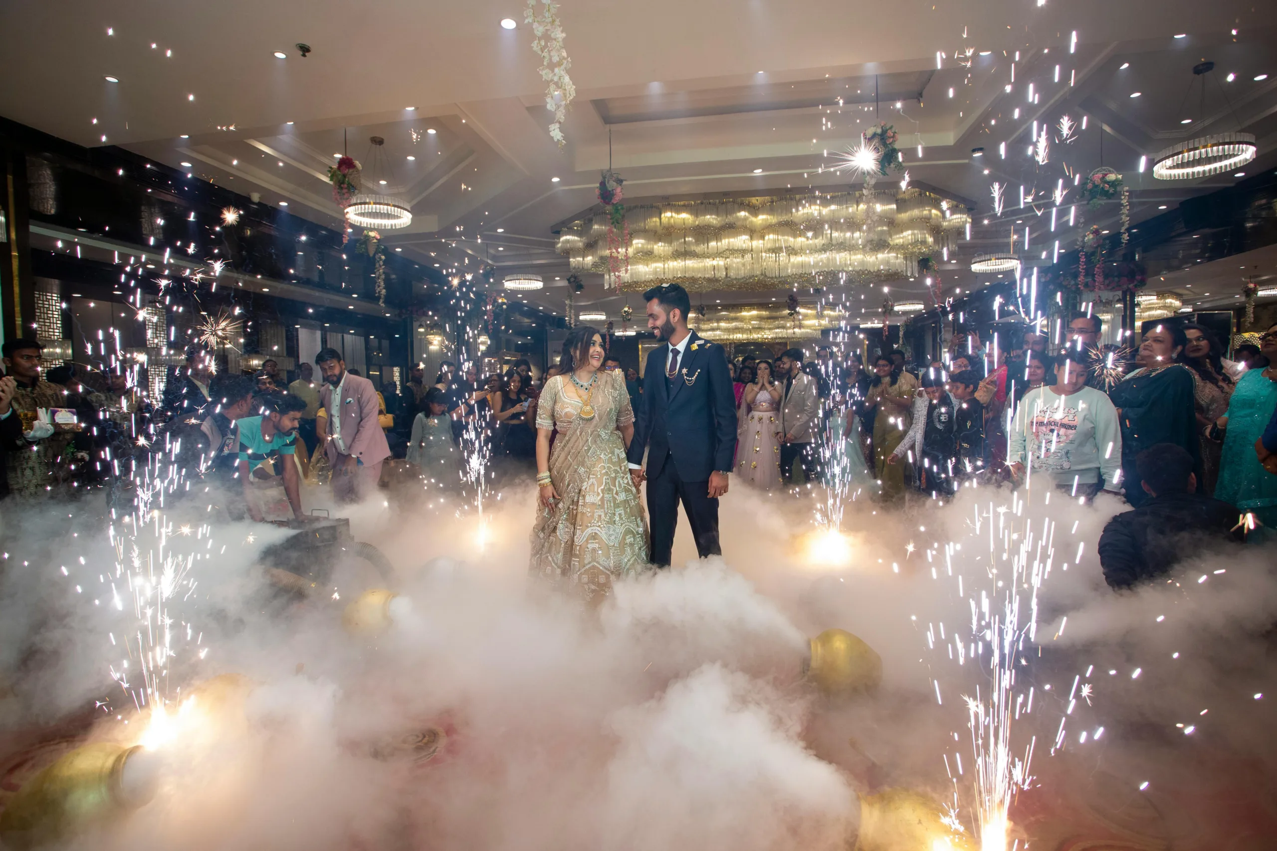 Bride and groom celebrating their wedding with guests amidst sparklers and smoke indoors.