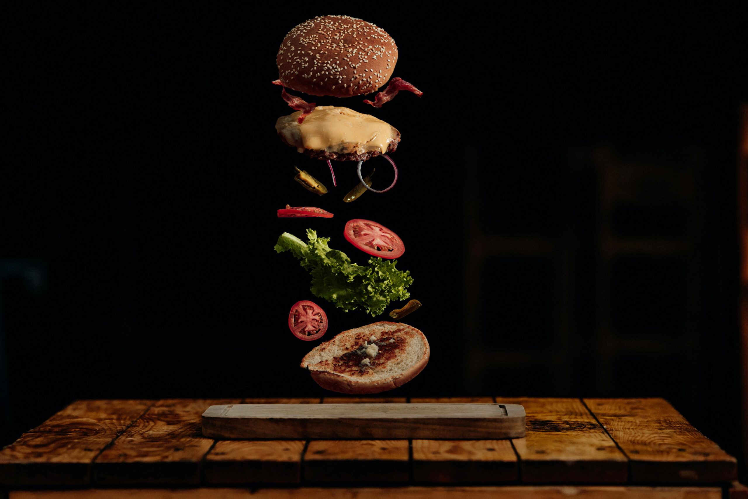 Visually striking deconstructed burger with floating ingredients in a dark background.