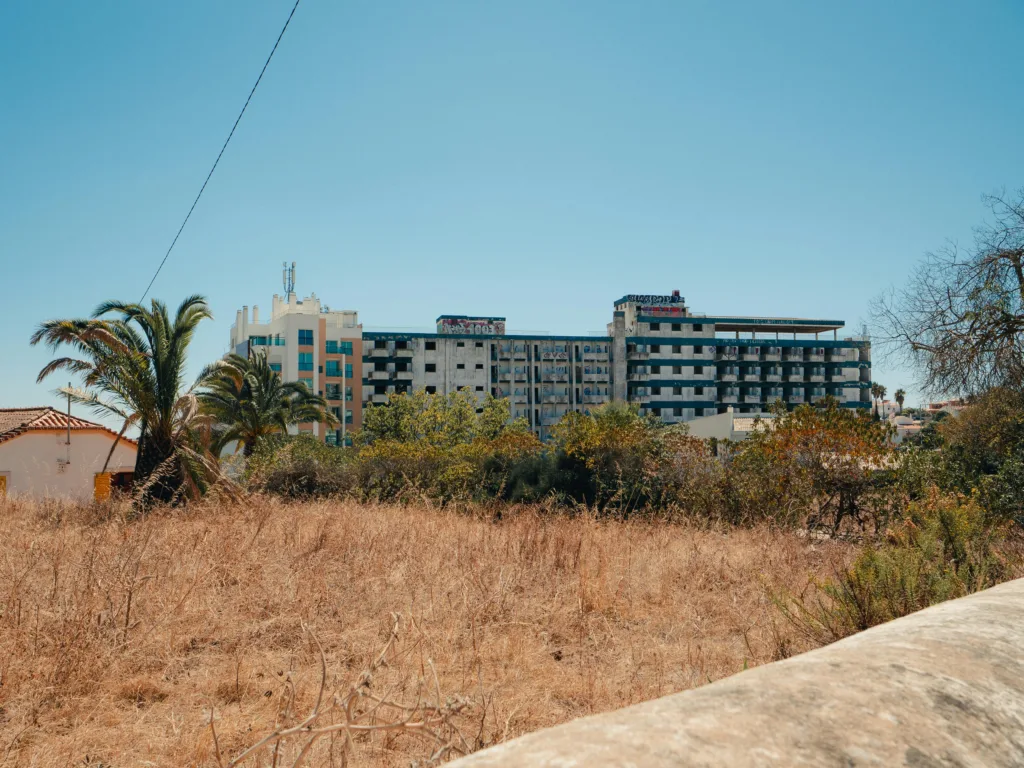 An abandoned hotel in Faro, Portugal, set against a sunlit, dry landscape with clear skies.